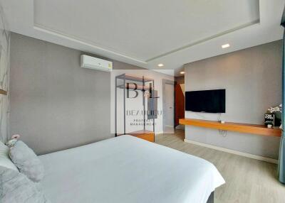 Modern bedroom interior with bed, wall-mounted TV, and wooden floating shelf