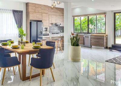 Modern kitchen with adjacent dining area, featuring wooden cabinetry, stainless steel appliances, and vibrant dining furniture.