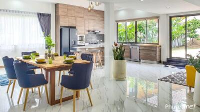 Modern kitchen with adjacent dining area, featuring wooden cabinetry, stainless steel appliances, and vibrant dining furniture.