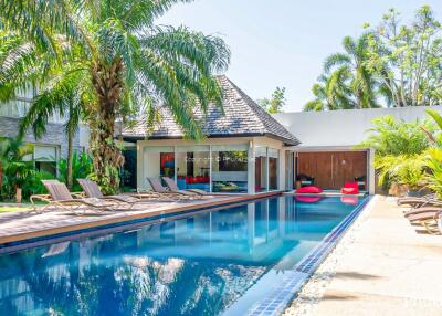 Luxurious swimming pool area in sunny weather with lounge chairs and palm trees