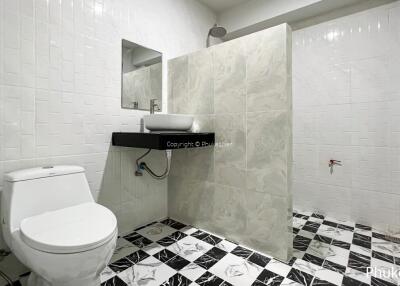 Modern bathroom with tiled walls and floor, featuring a toilet, sink, and spacious shower area.