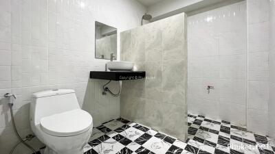 Modern bathroom with tiled walls and floor, featuring a toilet, sink, and spacious shower area.