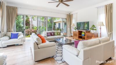 Spacious living room with large windows, white sofas, and a ceiling fan.