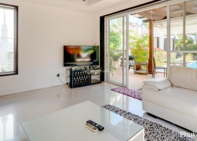 Bright living room with large windows, white sofa, coffee table, TV, and access to patio with pool view