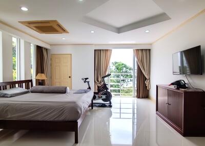 Spacious bedroom with large window, modern decor, exercise bike, and wall-mounted TV
