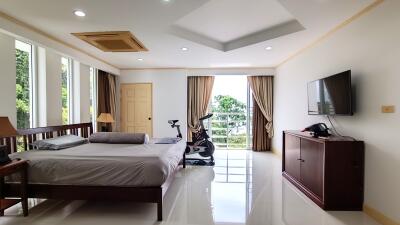 Spacious bedroom with large window, modern decor, exercise bike, and wall-mounted TV