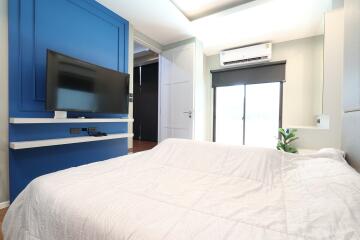 Bedroom with blue accent wall, TV, and white bedding