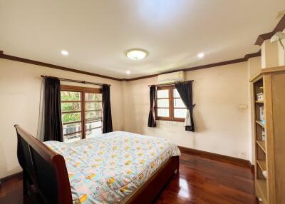 A well-lit bedroom with a large bed, wooden floor, and dark curtains.