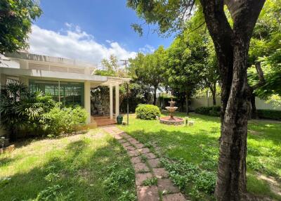 Beautiful garden with a pathway, greenery, and a fountain next to a house