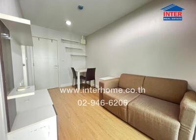 Living room with a brown sofa, white shelves, small dining table and chairs, and wooden flooring