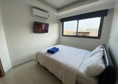 Bedroom with a wall-mounted television, bed, and a window with blinds