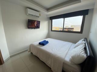 Bedroom with a wall-mounted television, bed, and a window with blinds