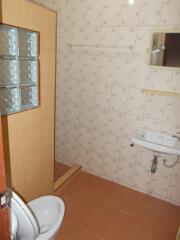 Bathroom with tiled walls and floor, featuring a small sink, mirror, toilet, and shower area with glass blocks