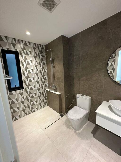 Modern bathroom with geometric tiled wall, shower, toilet, and vanity with round mirror