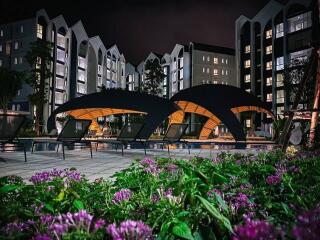 Modern apartment complex at night with well-lit exterior and poolside seating