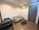 Cozy living room with wooden flooring, a gray sofa, small table, and an air conditioning unit.