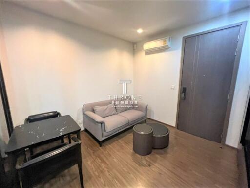 Cozy living room with wooden flooring, a gray sofa, small table, and an air conditioning unit.