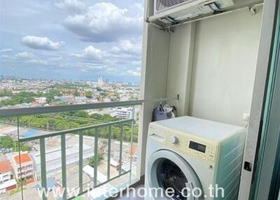 Laundry area with washing machine and external air conditioning unit, overlooking a city view from the balcony.