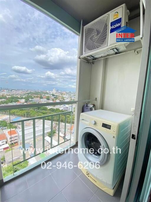 Laundry area with washing machine and external air conditioning unit, overlooking a city view from the balcony.