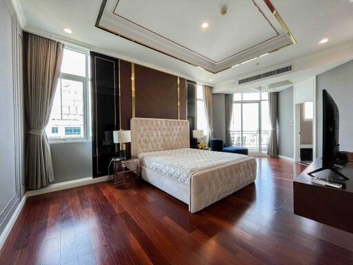 Spacious bedroom with large bed, wooden floor, modern decor, and natural light