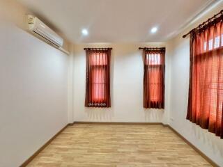 Bedroom with wooden floor, windows with dark curtains, and air conditioning unit