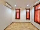 Bedroom with wooden floor, windows with dark curtains, and air conditioning unit