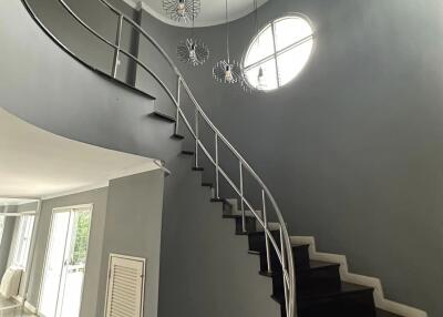 Elegant modern staircase with dark steps, curved metallic railing, and decorative light fixtures.