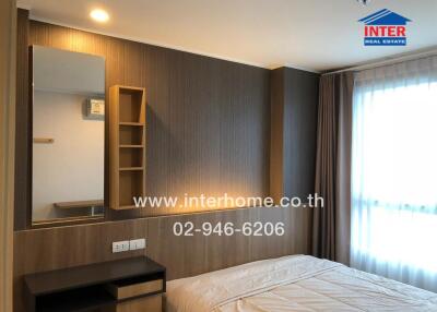 Modern bedroom with a large window, wooden furniture, mirror, and beige bedding.