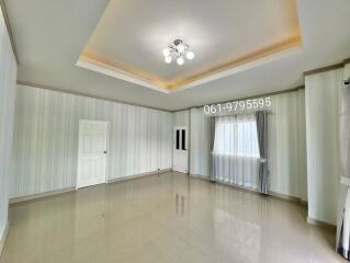 Spacious living room with a modern ceiling light, large window with curtains, tiled floor, and neutral-colored walls featuring wainscoting.