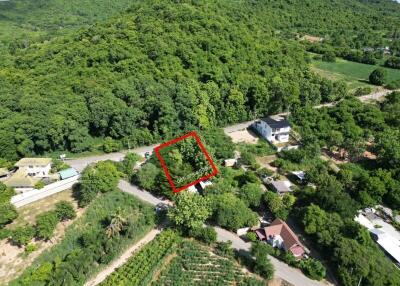 Aerial view of a green hilly area with houses and a marked plot