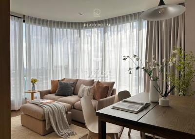 Spacious living room with large windows, beige sofa, wooden coffee table, and dining area.