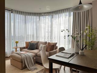 Spacious living room with large windows, beige sofa, wooden coffee table, and dining area.