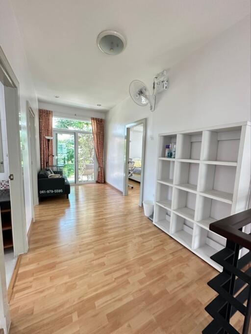 A bright hallway with wooden flooring, a large window, bookshelf, and a couch.