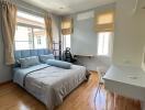 Modern bedroom with wooden floor, grey bedding, work desk and chair by windows