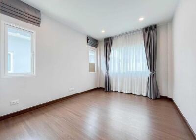 Well-lit empty room with wooden flooring and large window with curtains