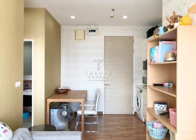 A living area with a view of the dining table, shelves, and washing machine.