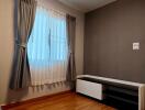 Bedroom with wooden flooring and window with curtains