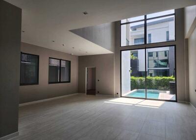 Spacious living room with large windows and high ceiling overlooking a swimming pool.