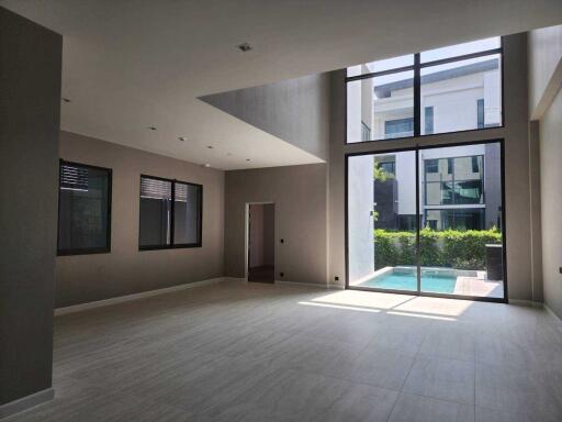 Spacious living room with large windows and high ceiling overlooking a swimming pool.