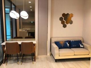 Modern living room and dining area with white sofa, decorative pillows, wooden dining table, and modern light fixtures.