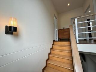 A staircase leading to an upper floor with wooden steps and a wall-mounted light fixture