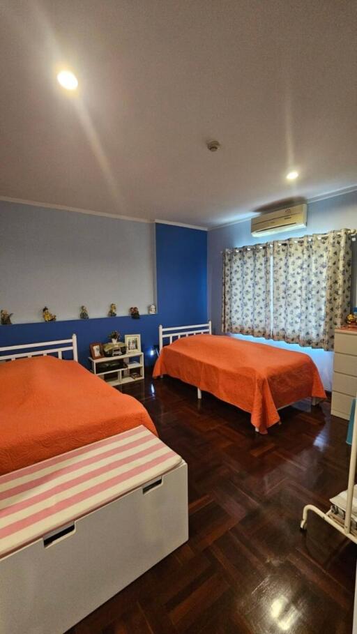 Two beds in a brightly decorated bedroom with hardwood floors and blue accent wall