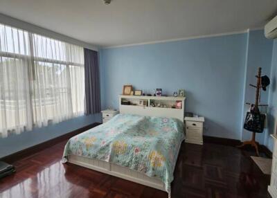 Well-lit bedroom with large windows, wooden flooring, and pastel blue walls