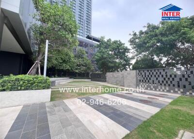 Outdoor area with modern pavement, greenery, and a tall building.