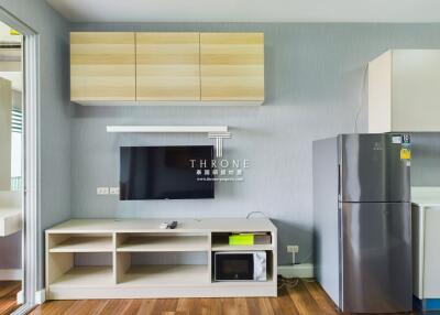 Modern living room with mounted television, wooden flooring, and kitchen appliances.