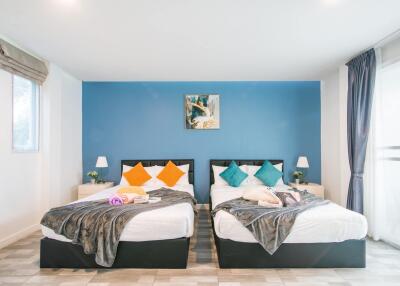 Modern bedroom with two double beds, blue accent wall, and natural light