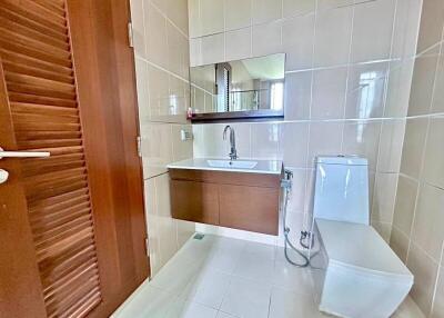 Modern bathroom with wooden door, wall-mounted vanity, large mirror, and toilet