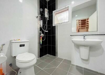 Modern bathroom with white toilet, sink, and shower area featuring dark tiles