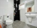 Modern bathroom with white toilet, sink, and shower area featuring dark tiles