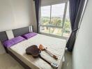 Bedroom with a large window and a bed with two purple pillows